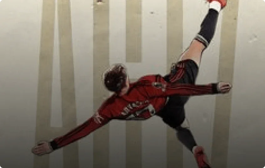 Football player in a red and black outfit performing a flip against a striped wall.